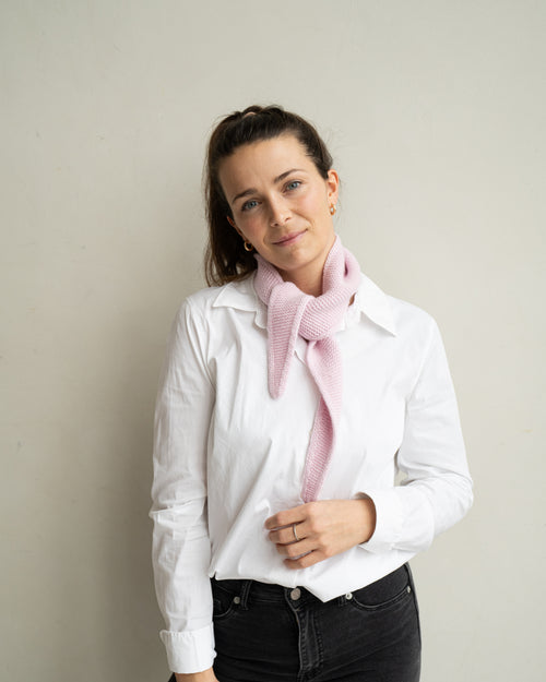 eine frau schaut zur seite und trägt einen mini schal aus merinowolle in der farbe pink