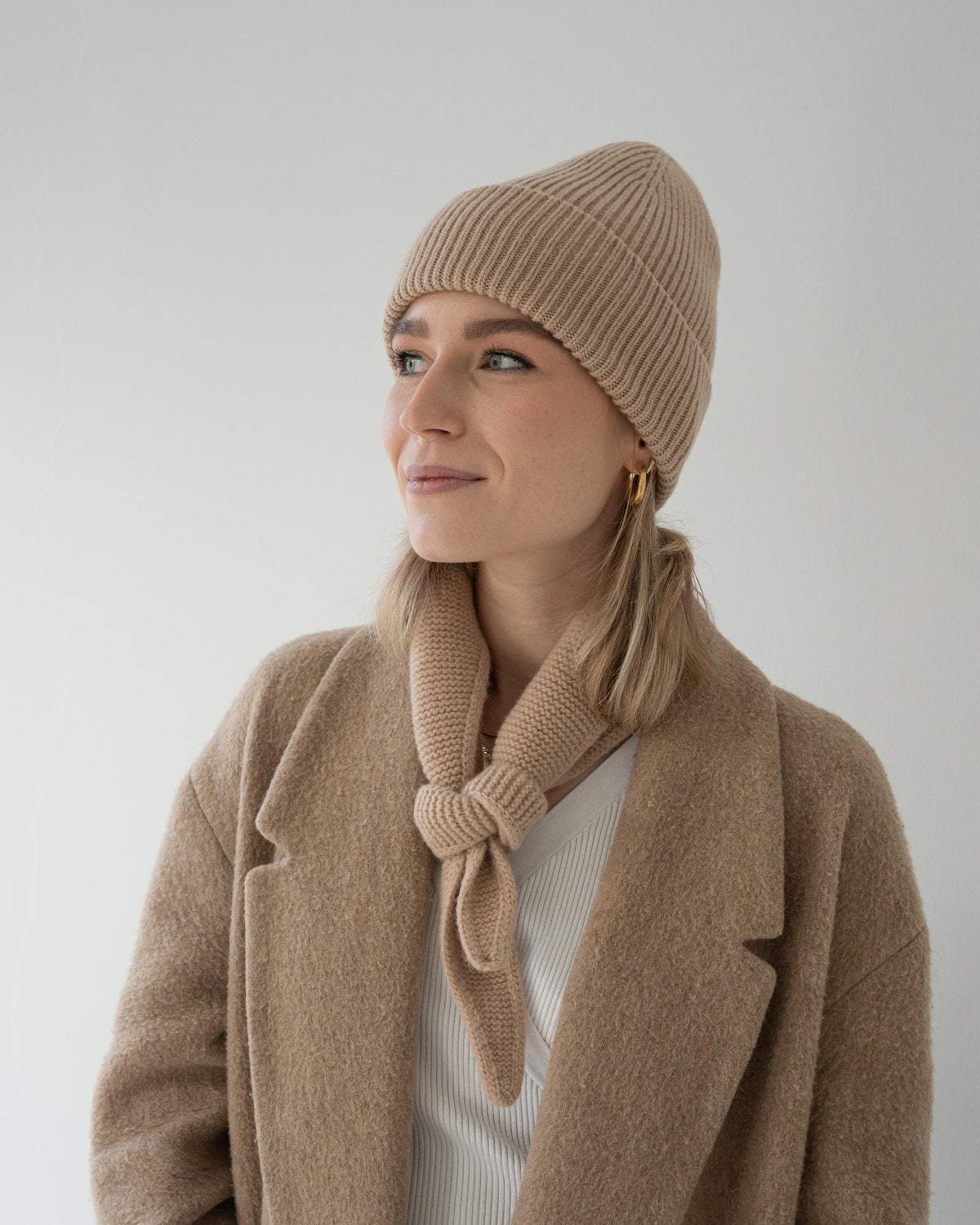 eine frau trägt eine muetze und einen mini schal aus merinowolle in beige